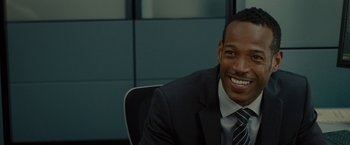 Movie still from “The Heat” (2013), directed by Paul Feig – A man in a suit and tie smiling for the camera; Close Up shot, Over the shoulder angle
