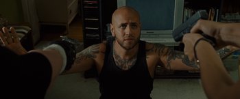 Movie still from “The Heat” (2013), directed by Paul Feig – A bald man with tattoos is sitting in a living room; Close Up shot, Low angle