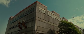 Movie still from “The Heat” (2013), directed by Paul Feig – An industrial building with a sky in the background; Extreme Wide shot, Low angle
