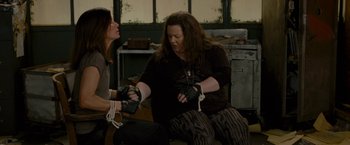 Movie still from “The Heat” (2013), directed by Paul Feig – Two women are holding hands while one of them is tied to a chair; Medium shot, High angle