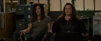 Movie still from “The Heat” (2013), directed by Paul Feig – A couple of women standing next to each other in a room; Medium shot, High angle