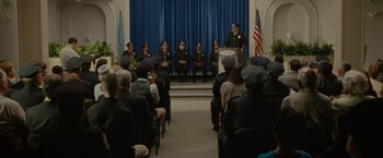 Movie still from “The Heat” (2013), directed by Paul Feig – A group of people sitting and standing in front of a podium; Wide shot, Over the shoulder angle