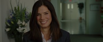 Movie still from “The Heat” (2013), directed by Paul Feig – A woman with long dark brown hair smiling for the camera; Close Up shot, Over the shoulder angle