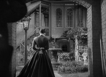 Movie still from “The Heiress” (1949), directed by William Wyler – An old photo of a woman standing in front of a building; Wide shot, Low angle