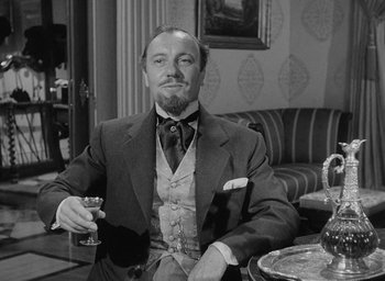 Movie still from “The Heiress” (1949), directed by William Wyler – A black and white photo of a man sitting at a table with a glass of wine; Medium shot, Low angle