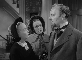 Movie still from “The Heiress” (1949), directed by William Wyler – Two women and a man are standing in a room; Medium shot, Over the shoulder angle