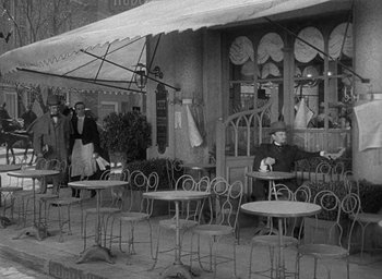 Movie still from “The Heiress” (1949), directed by William Wyler – An old photo of people sitting at tables outside a restaurant; Wide shot, High angle