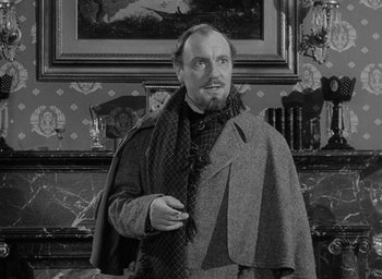 Movie still from “The Heiress” (1949), directed by William Wyler – A man in a suit and a scarf is standing in front of a fireplace; Medium shot, Over the shoulder angle