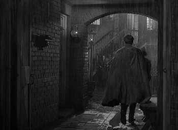 Movie still from “The Heiress” (1949), directed by William Wyler – A man wearing a cape walking down a dark alley way; Wide shot, High angle