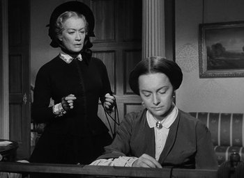 Movie still from “The Heiress” (1949), directed by William Wyler – Two women are sitting at a desk in a room; Medium shot, Over the shoulder angle