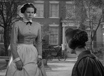 Movie still from “The Heiress” (1949), directed by William Wyler – A woman wearing a dress and a hat standing in front of a woman; Medium shot, Over the shoulder angle
