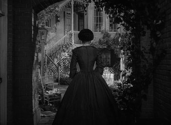 Movie still from “The Heiress” (1949), directed by William Wyler – A woman in a long black dress standing in front of a house; Wide shot, Over the shoulder angle