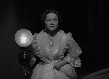 Movie still from “The Heiress” (1949), directed by William Wyler – A woman dressed in period clothing holding a lamp; Medium shot, High angle