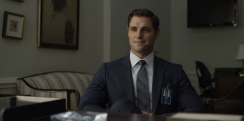 Movie still from “House of Cards” (2013), created by Beau Willimon – A man in a suit and tie sitting in front of a table; Medium shot, Over the shoulder angle