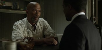 Movie still from “House of Cards” (2013), created by Beau Willimon – A man sitting at a table talking to another man in front of him; Close Up shot, Over the shoulder angle