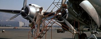 Movie still from “The High and the Mighty” (1954), directed by William A. Wellman – A man in a white suit walking up a ladder to an airplane on a runway; Wide shot, Low angle