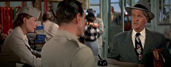 Movie still from “The High and the Mighty” (1954), directed by William A. Wellman – A man sitting at a table in front of other people; Medium shot, Over the shoulder angle