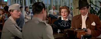Movie still from “The High and the Mighty” (1954), directed by William A. Wellman – A woman sitting at a table in front of a man; Medium shot, Over the shoulder angle