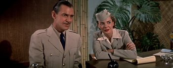 Movie still from “The High and the Mighty” (1954), directed by William A. Wellman – A man and a woman sitting at a table in front of a bamboo wall; Medium shot, Low angle