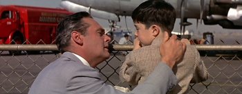 Movie still from “The High and the Mighty” (1954), directed by William A. Wellman – A man and a boy are holding each other in front of a chain link fence; Close Up shot, Low angle