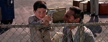 Movie still from “The High and the Mighty” (1954), directed by William A. Wellman – A young boy holding a gun next to an older man; Close Up shot, Over the shoulder angle