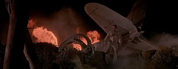 Movie still from “The High and the Mighty” (1954), directed by William A. Wellman – A man walking next to an airplane in front of fire; Wide shot, Low angle