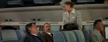 Movie still from “The High and the Mighty” (1954), directed by William A. Wellman – An airline stewardess talking to passengers on a plane; Medium shot, Over the shoulder angle