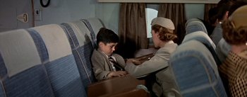 Movie still from “The High and the Mighty” (1954), directed by William A. Wellman – An older woman is helping a young boy to sit in a chair; Medium shot, High angle