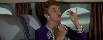 Movie still from “The High and the Mighty” (1954), directed by William A. Wellman – A woman in a purple dress is holding a bottle of perfume; Close Up shot, Low angle