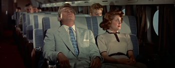 Movie still from “The High and the Mighty” (1954), directed by William A. Wellman – A man and two women sitting next to each other on a plane; Medium shot, Overhead angle