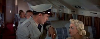 Movie still from “The High and the Mighty” (1954), directed by William A. Wellman – A man in a uniform talking to a woman in an airplane; Medium shot, Over the shoulder angle