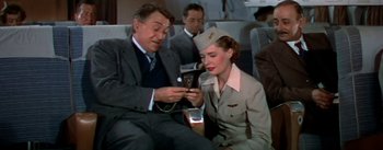 Movie still from “The High and the Mighty” (1954), directed by William A. Wellman – A man and a woman looking at a cell phone on a plane; Medium shot, High angle