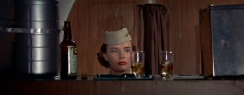 Movie still from “The High and the Mighty” (1954), directed by William A. Wellman – A woman with a hat on sitting in front of two glasses of whiskey; Medium shot, Low angle