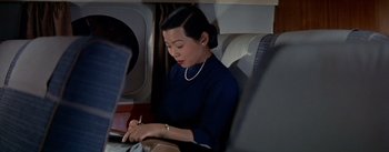 Movie still from “The High and the Mighty” (1954), directed by William A. Wellman – A woman sitting on top of an airplane writing on a piece of paper; Medium shot, High angle