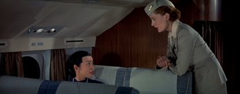 Movie still from “The High and the Mighty” (1954), directed by William A. Wellman – A woman in a uniform talking to another woman in an airplane; Medium shot, Low angle