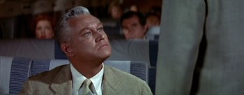 Movie still from “The High and the Mighty” (1954), directed by William A. Wellman – An older man in a suit and tie sitting on a plane; Close Up shot, Low angle