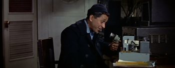 Movie still from “The High and the Mighty” (1954), directed by William A. Wellman – A man in a hat and coat holding a camera; Medium shot, High angle