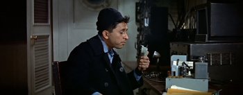 Movie still from “The High and the Mighty” (1954), directed by William A. Wellman – A man holding a cell phone while sitting at a table; Medium shot, High angle