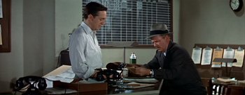 Movie still from “The High and the Mighty” (1954), directed by William A. Wellman – Two men are sitting at a desk looking at a cell phone; Medium shot, High angle