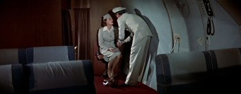 Movie still from “The High and the Mighty” (1954), directed by William A. Wellman – A man and a woman in uniforms shake hands; Wide shot, Overhead angle