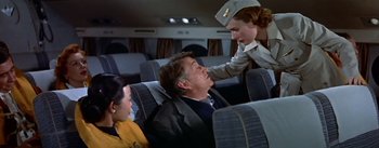 Movie still from “The High and the Mighty” (1954), directed by William A. Wellman – A woman in a nurse's uniform touching the head of a man on a plane; Medium shot, High angle