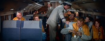 Movie still from “The High and the Mighty” (1954), directed by William A. Wellman – A man in a uniform standing next to a woman in an airplane; Medium shot, High angle