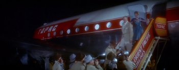 Movie still from “The High and the Mighty” (1954), directed by William A. Wellman – A group of people standing around a red and white airplane; Wide shot, Low angle
