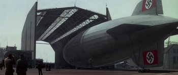Movie still from “The Hindenburg” (1975), directed by Robert Wise – A large black and white airplane sitting on top of an airport runway; Extreme Wide shot, Low angle