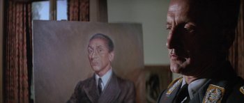 Movie still from “The Hindenburg” (1975), directed by Robert Wise – A man standing in front of a painting of a man; Close Up shot, Low angle