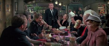 Movie still from “The Hindenburg” (1975), directed by Robert Wise – A group of people sitting around a table eating food; Medium shot, Over the shoulder angle