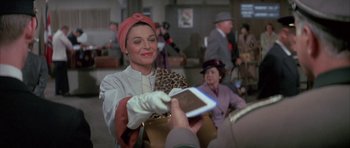 Movie still from “The Hindenburg” (1975), directed by Robert Wise – An older woman is handing a purse to a man; Medium shot, Over the shoulder angle