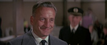 Movie still from “The Hindenburg” (1975), directed by Robert Wise – An older man wearing a suit and tie smiling; Close Up shot, Low angle