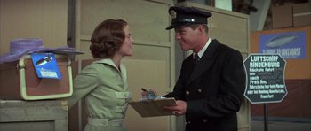 Movie still from “The Hindenburg” (1975), directed by Robert Wise – A man and a woman are holding a clipboard; Medium shot, Over the shoulder angle