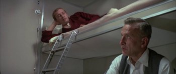 Movie still from “The Hindenburg” (1975), directed by Robert Wise – A man sitting on top of a bed next to another man; Medium shot, Low angle